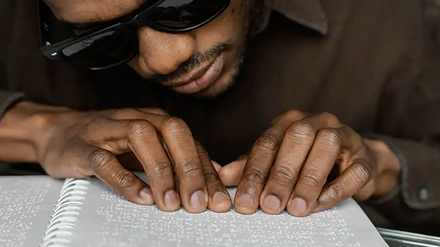 A blind man wearing dark glasses reading a braille document.